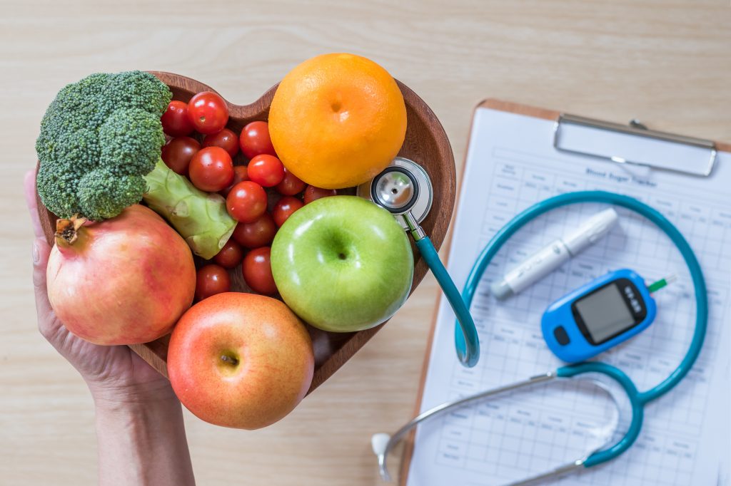Diabetes monitor, Cholesterol diet and healthy food eating nutritional concept with clean fruits in nutritionist's heart dish and patient's blood sugar control record with diabetic measuring tool kit